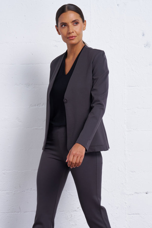 Woman wearing a dark gray suit against a white brick wall