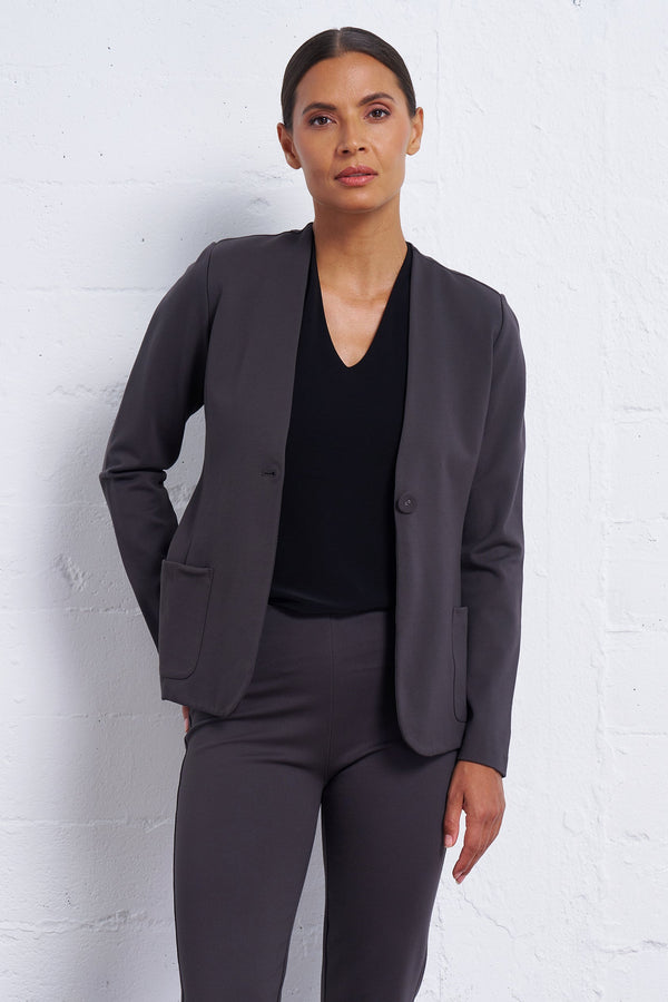 Woman wearing a gray suit against a white brick wall